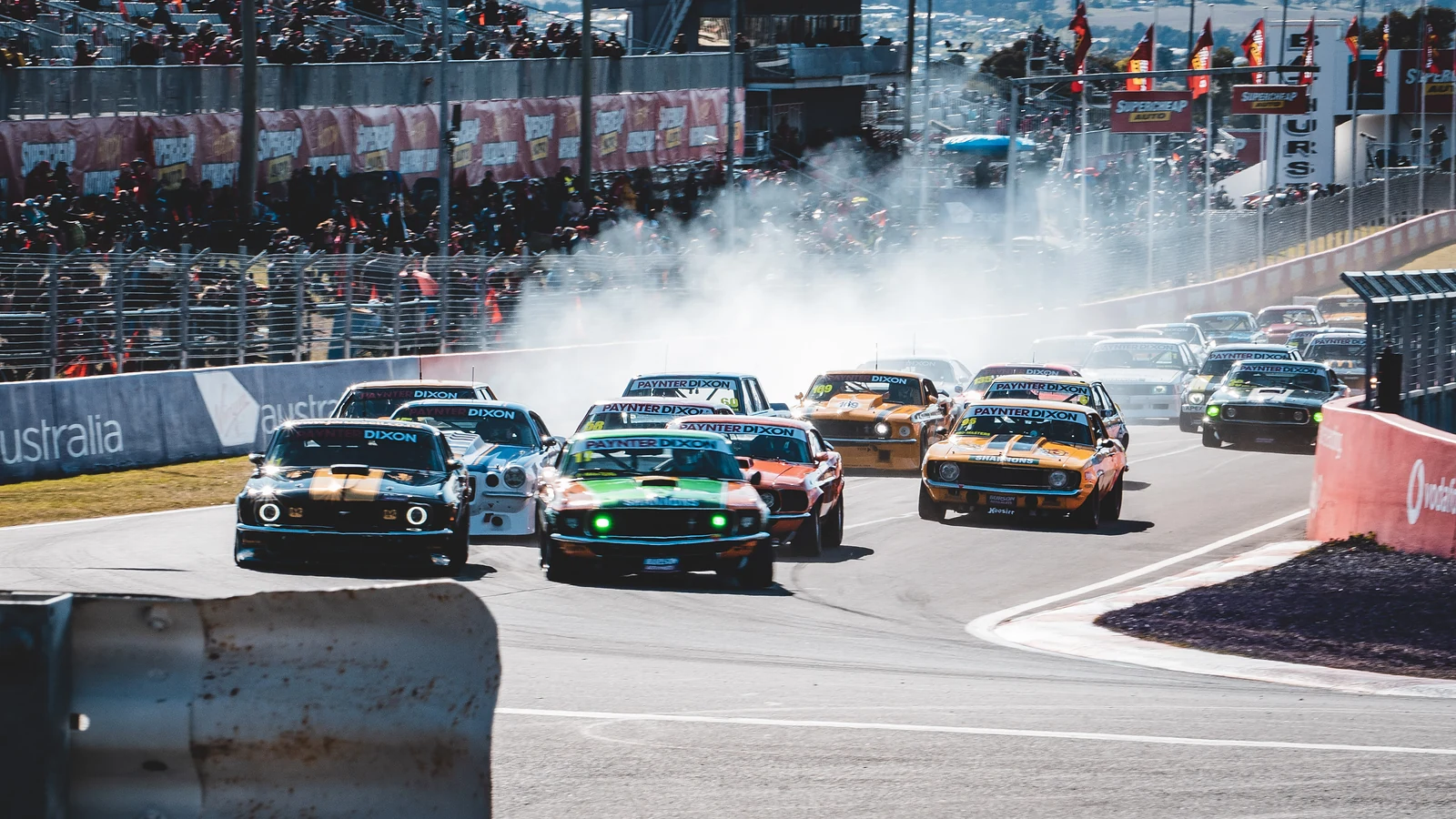 Pack of race cars sliding through a corner in tyre smoke at Bathurst