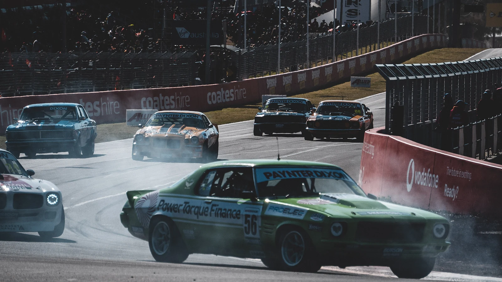 Green muscle car kicking up tyre smoke at a corner at Bathurst