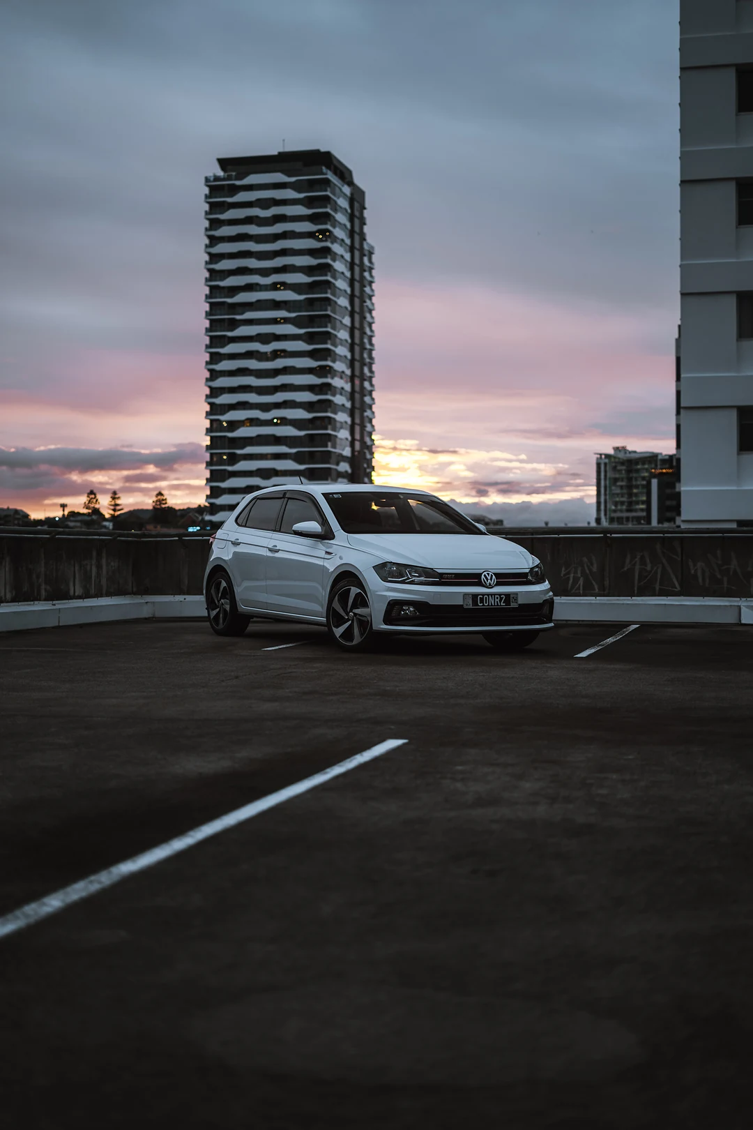 White Volkswagen Polo on a rooftop car park under a pink sunset sky