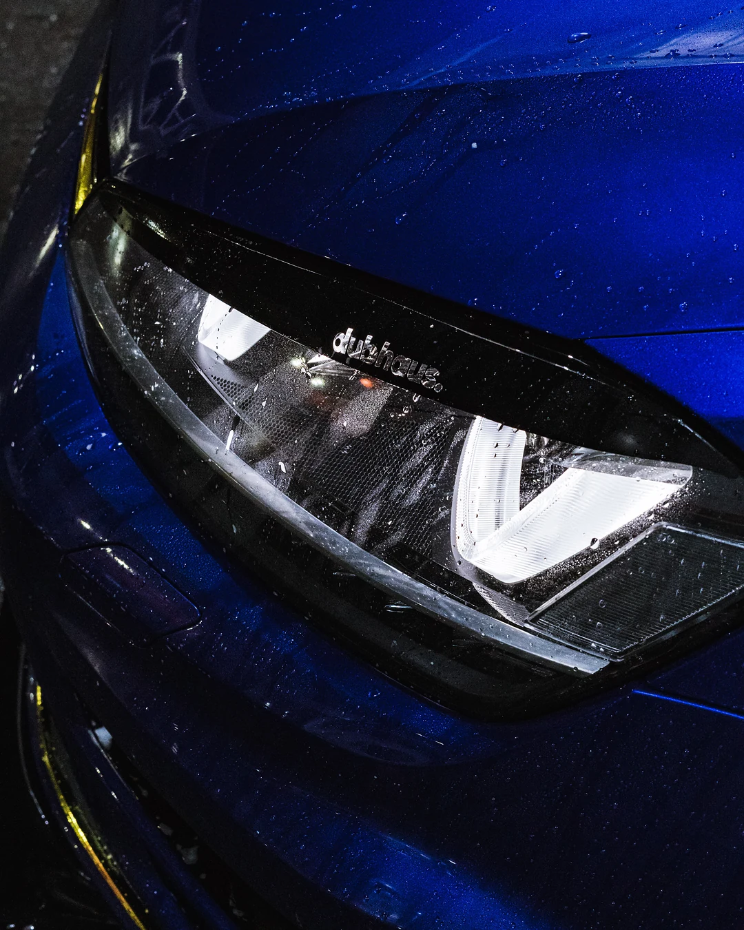Headlight of a blue Volkswagen Golf covered in water droplets