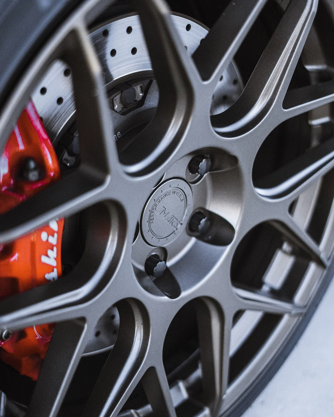 Red brake caliper behind a grey multi-spoke wheel, close up