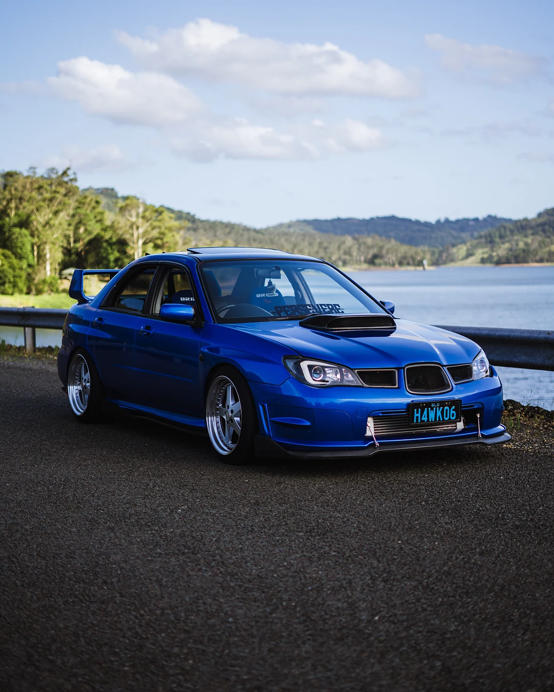 Blue Subaru Impreza WRX front three-quarter by a lake under a blue sky