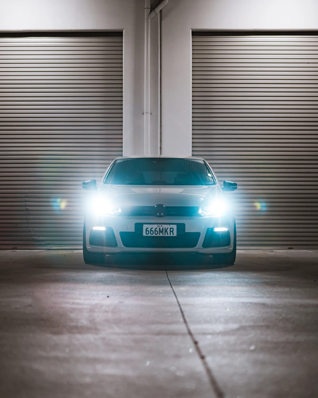White Golf R facing the camera in front of two roller doors, headlights glowing