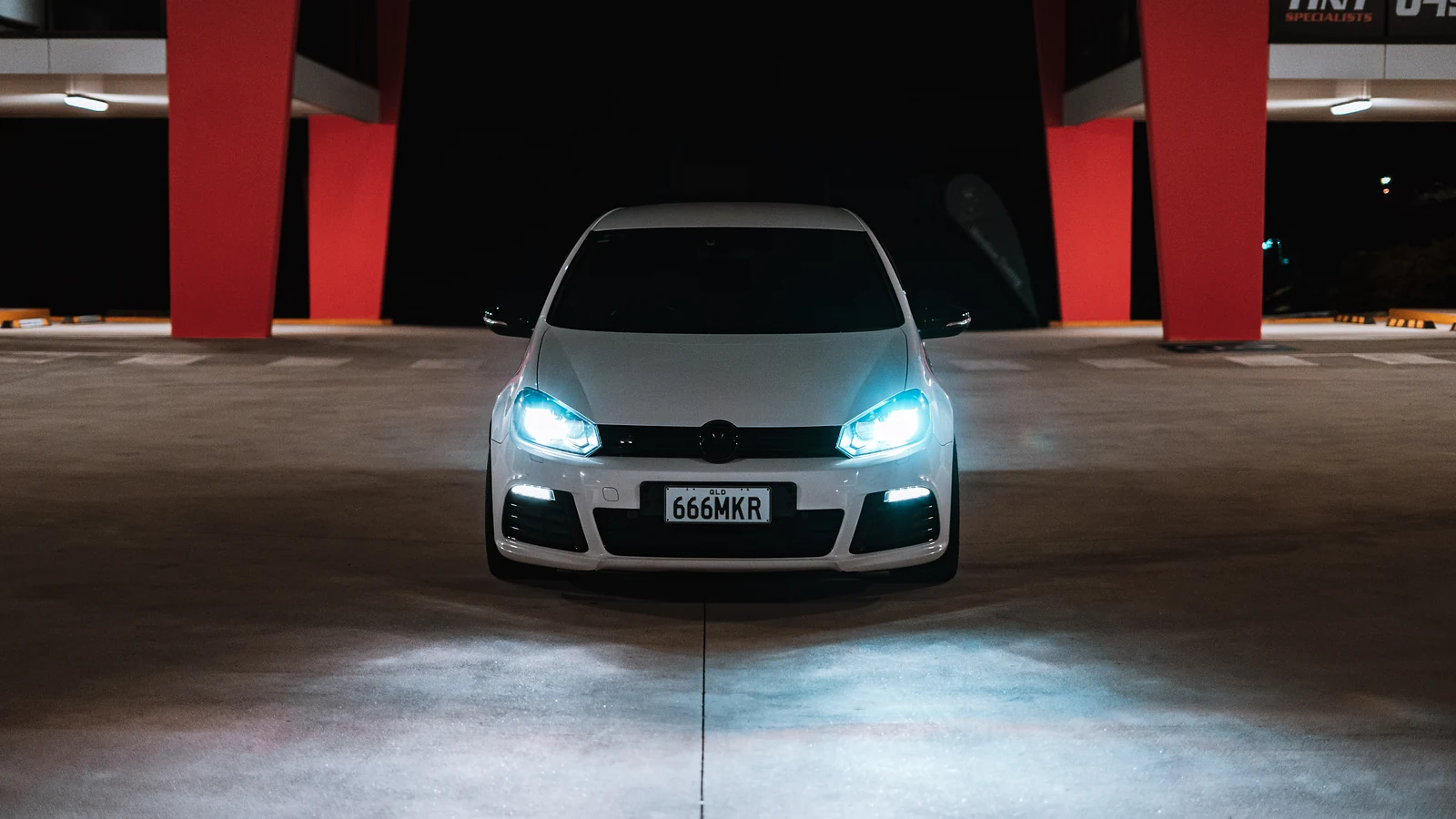 White Golf R head-on between red pillars in a car park at night, headlights on