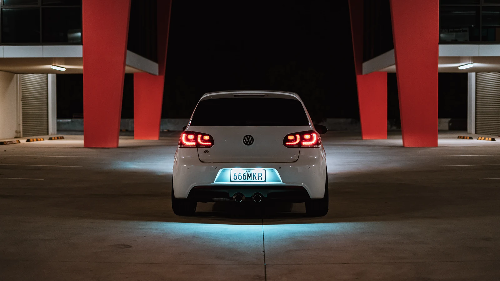 White Golf R from behind between red pillars at night, tail lights and blue underglow