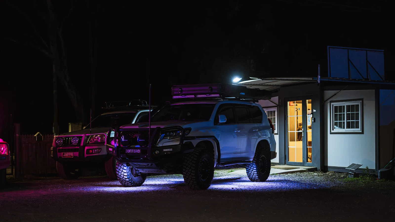 4WDs lit with purple and blue underglow outside a building at night