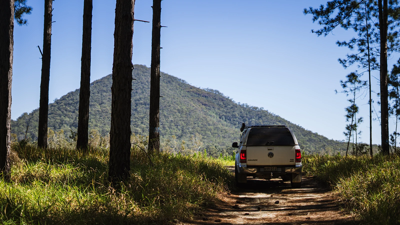 4WD ute on a grassy track below a mountain on a clear day
