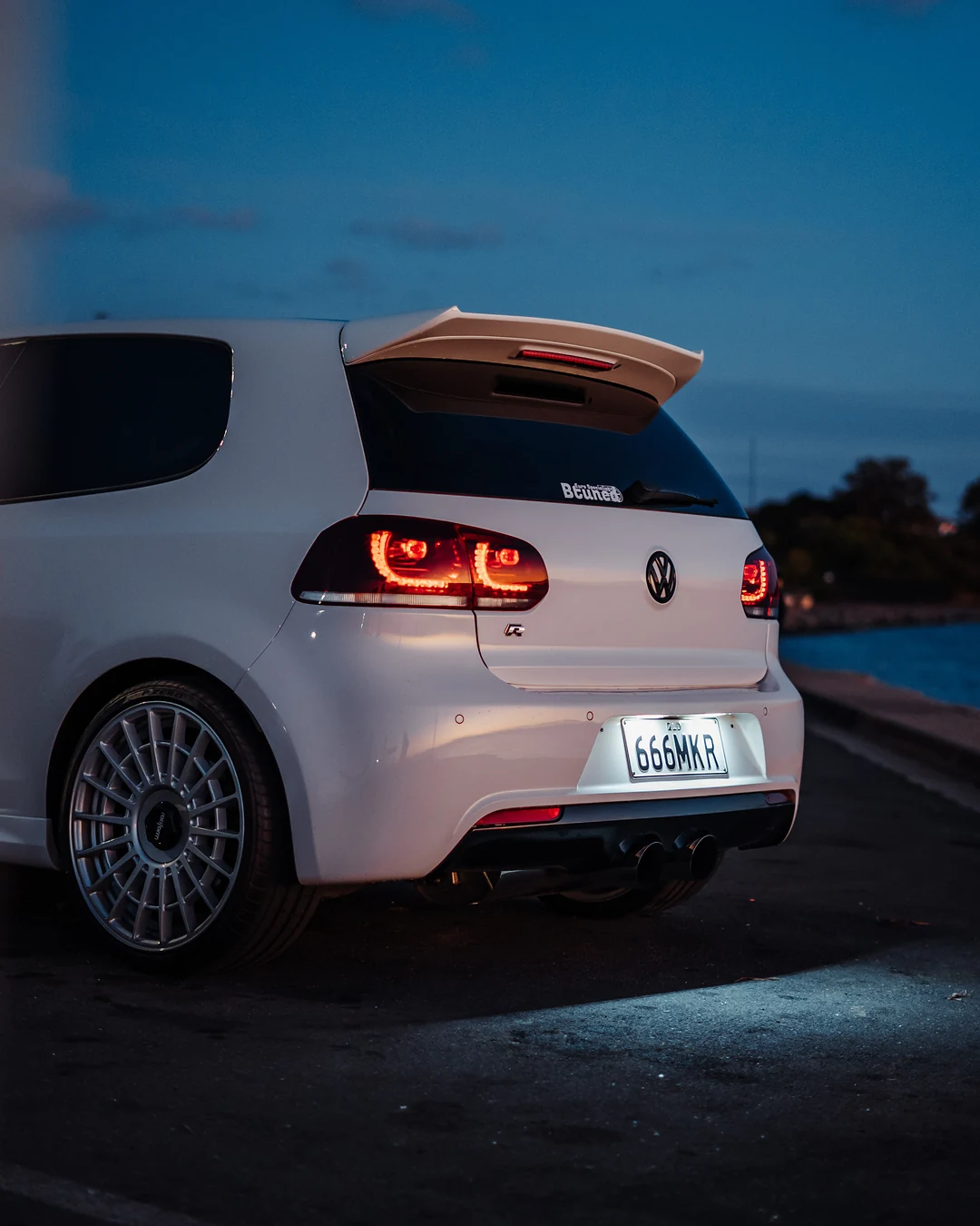 White Golf from behind at dusk, tail lights glowing against a deep blue sky