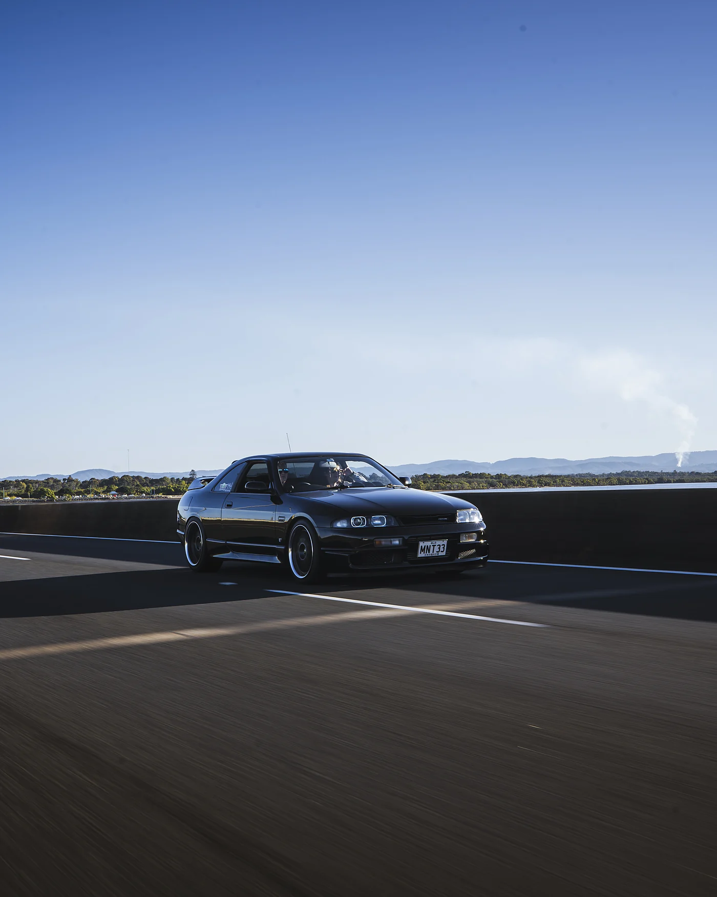 Dark coupe on an open road under a clear blue sky