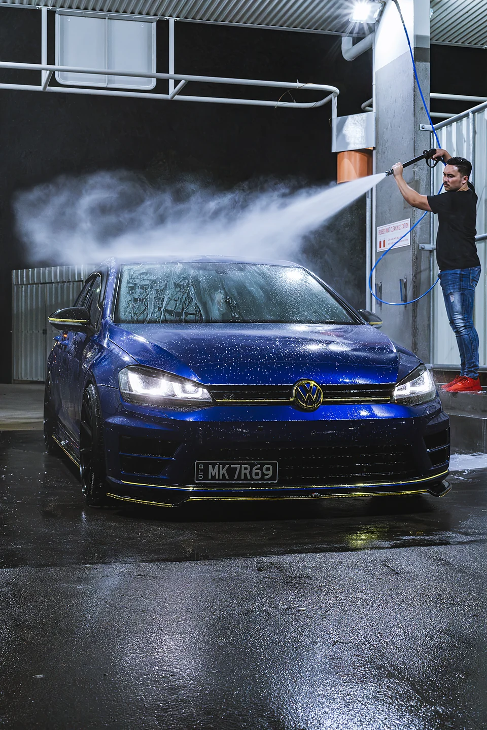 Blue Volkswagen Golf being rinsed at a car wash at night