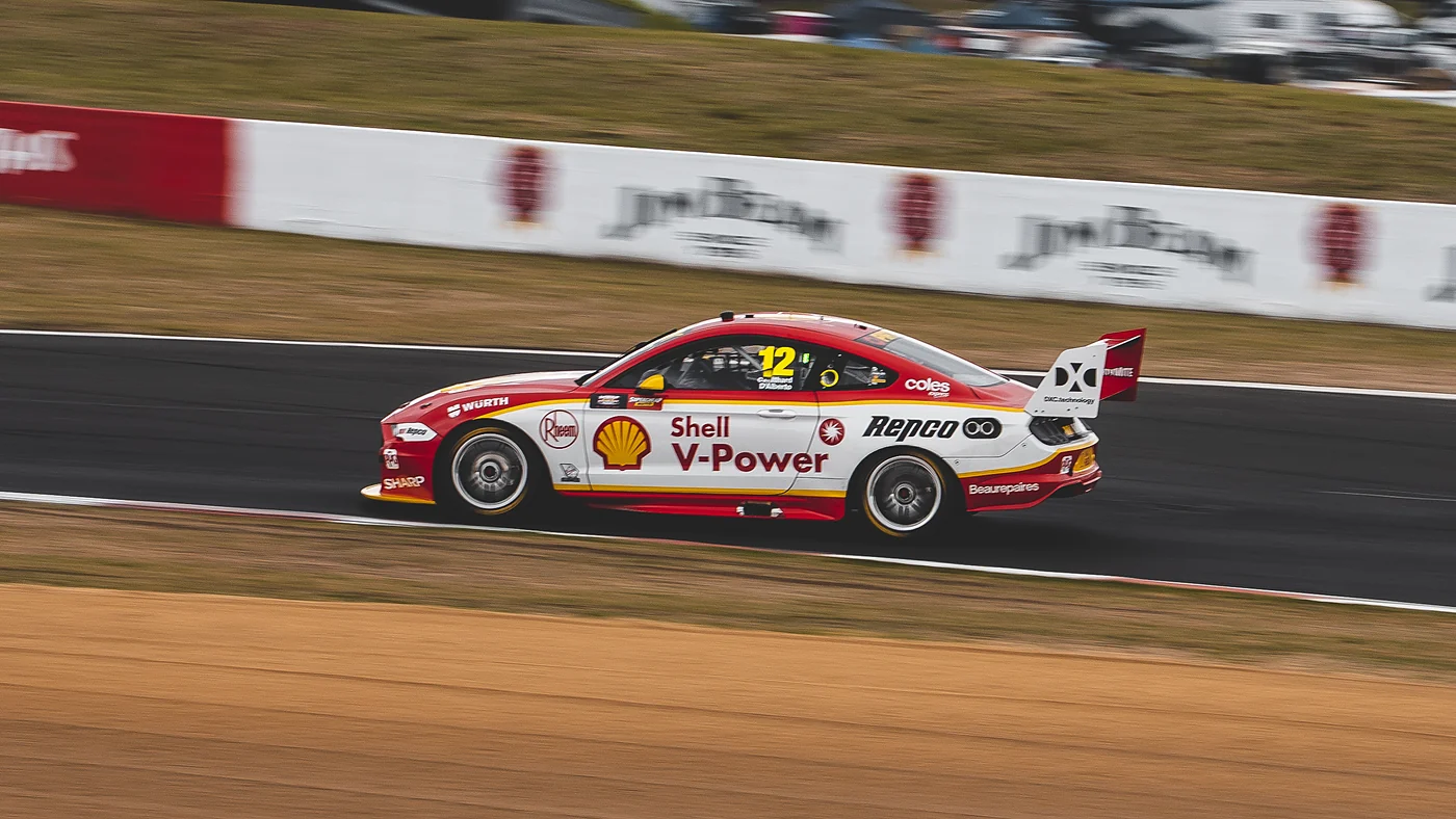 Red race car at speed past the pit wall, panned so the background blurs